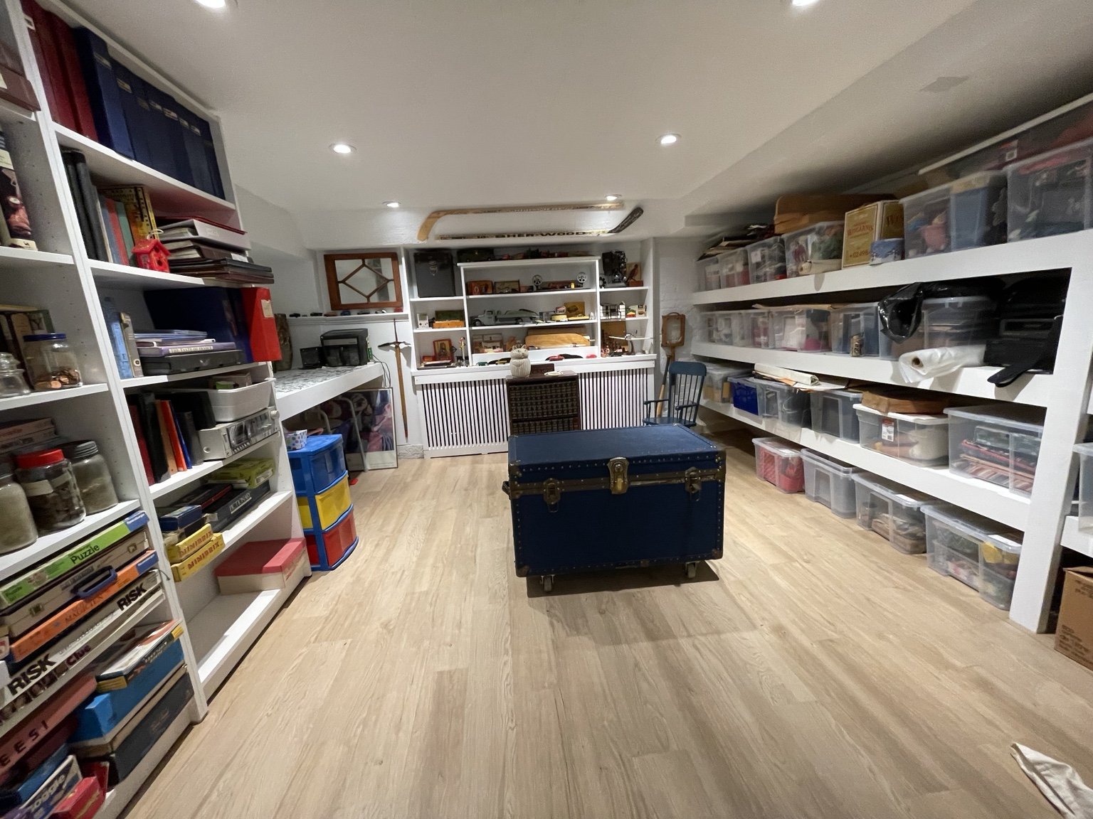 Organized basement collection room with white shelving, display cabinets and an antique blue trunk
