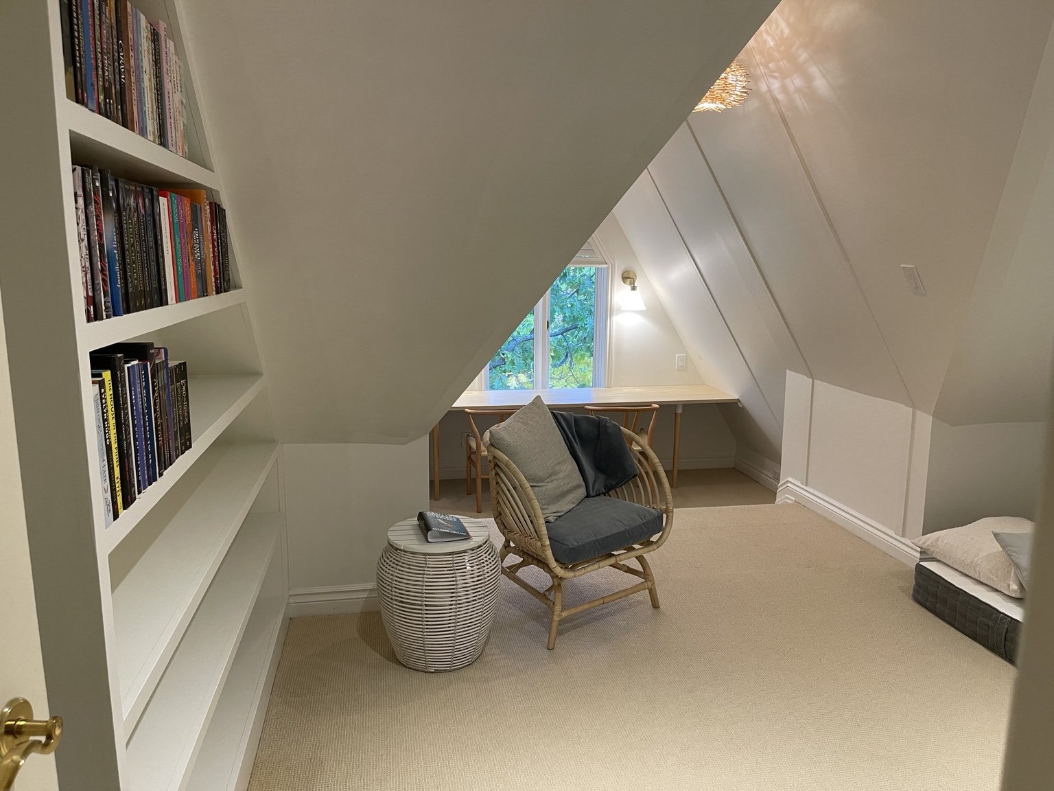 Custom white library shelves fitted beneath an angled roof beside a reading chair